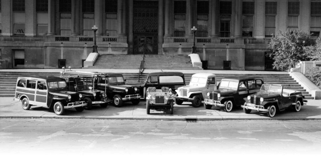 Vintage Jeep models parked in front of a historic building with grand stairs.