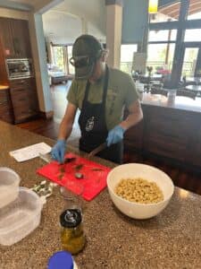 Person in a kitchen preparing a meal with pasta, wearing gloves and an apron.
