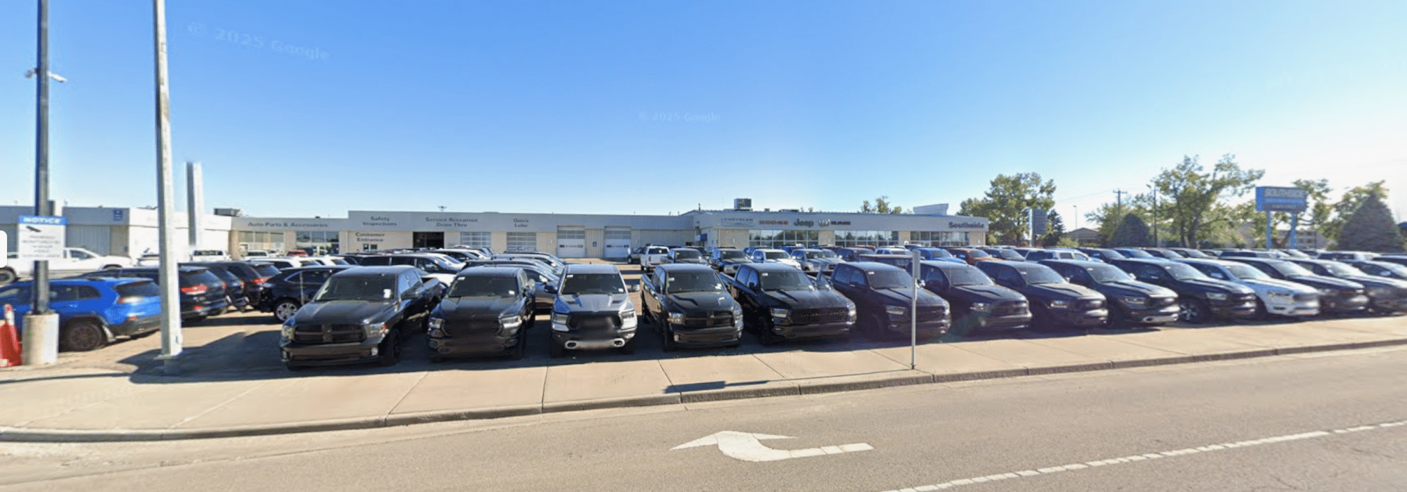 Car dealership lot with numerous parked vehicles, set against a backdrop of the dealership building.