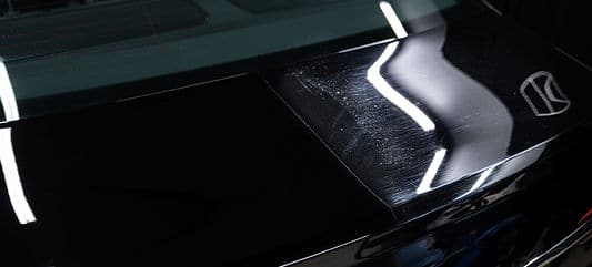 Black car hood showing before and after paint correction