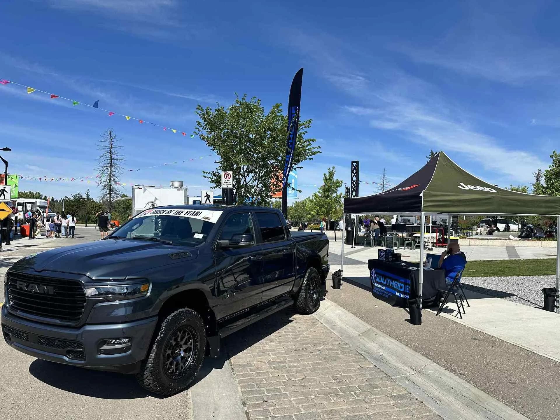 Black Ram truck displayed at an outdoor auto event with a canopy and people in the background.