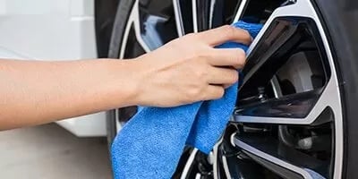 Hand cleaning a car wheel with a blue microfiber cloth.