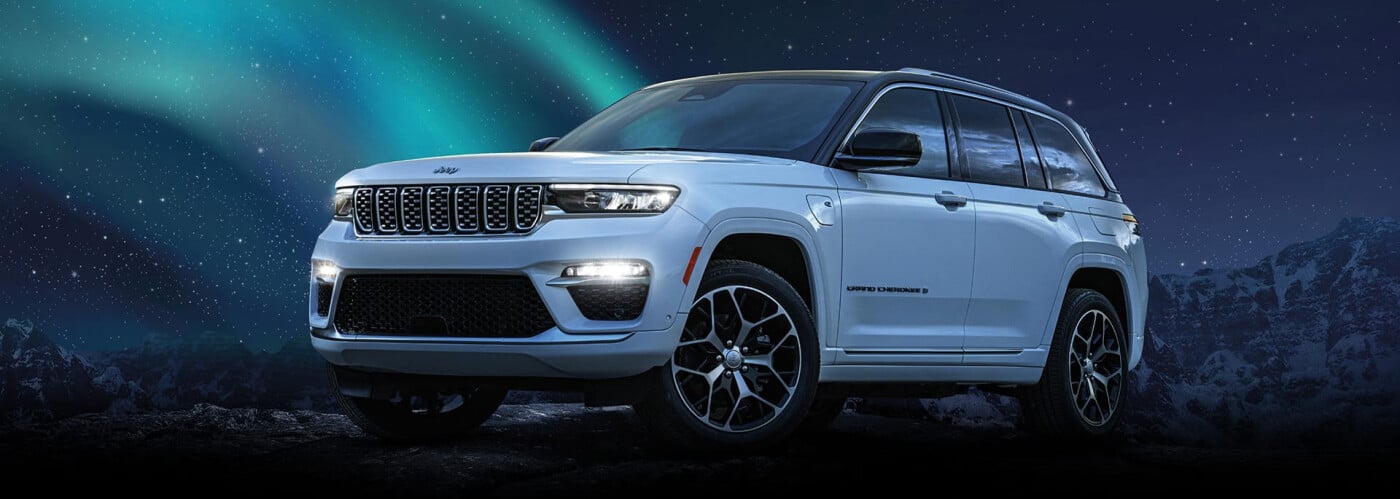 White SUV parked under northern lights and starry sky, with mountainous landscape.