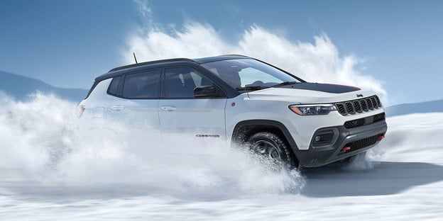 White SUV maneuvering through snow, showcasing its off-road capabilities under a clear blue sky.