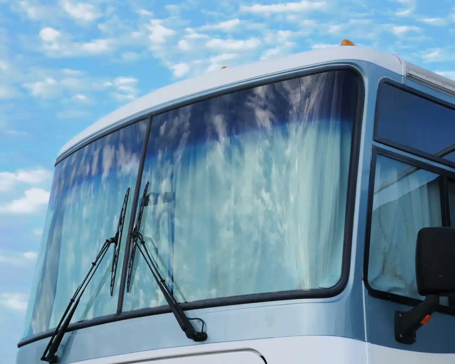 Close-up of a bus windshield with wipers against a blue sky backdrop.