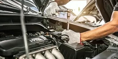 Mechanic with gloves using tools to fix car engine under open hood.