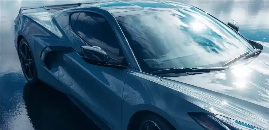 Sleek blue sports car reflecting the sky, parked on a wet surface.
