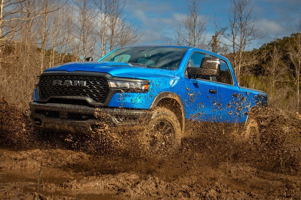 A blue Ram truck driving through muddy terrain, showcasing off-road capabilities under a clear sky.