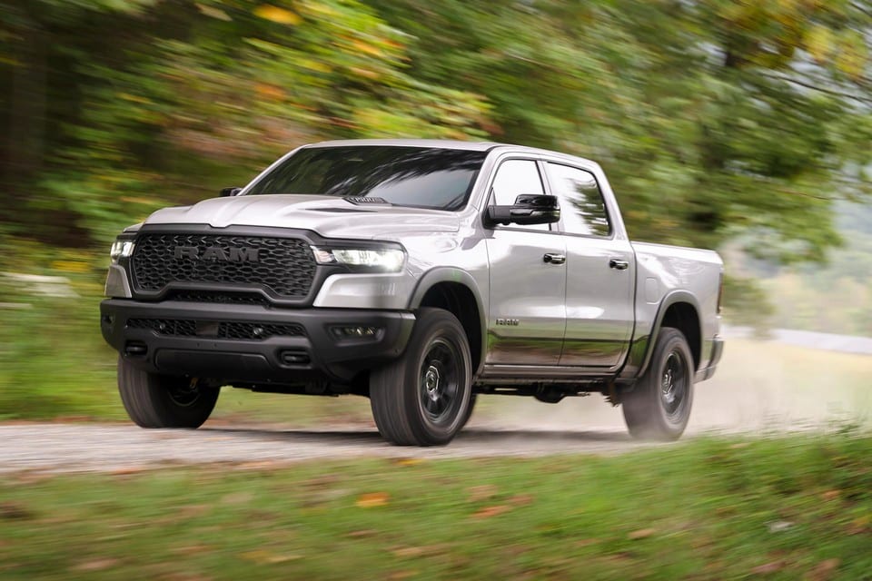 Silver pickup truck driving on a gravel road through a lush green forest.