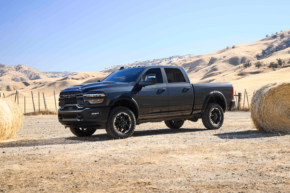 Black pickup truck parked between hay bales in a rural landscape under a clear blue sky.