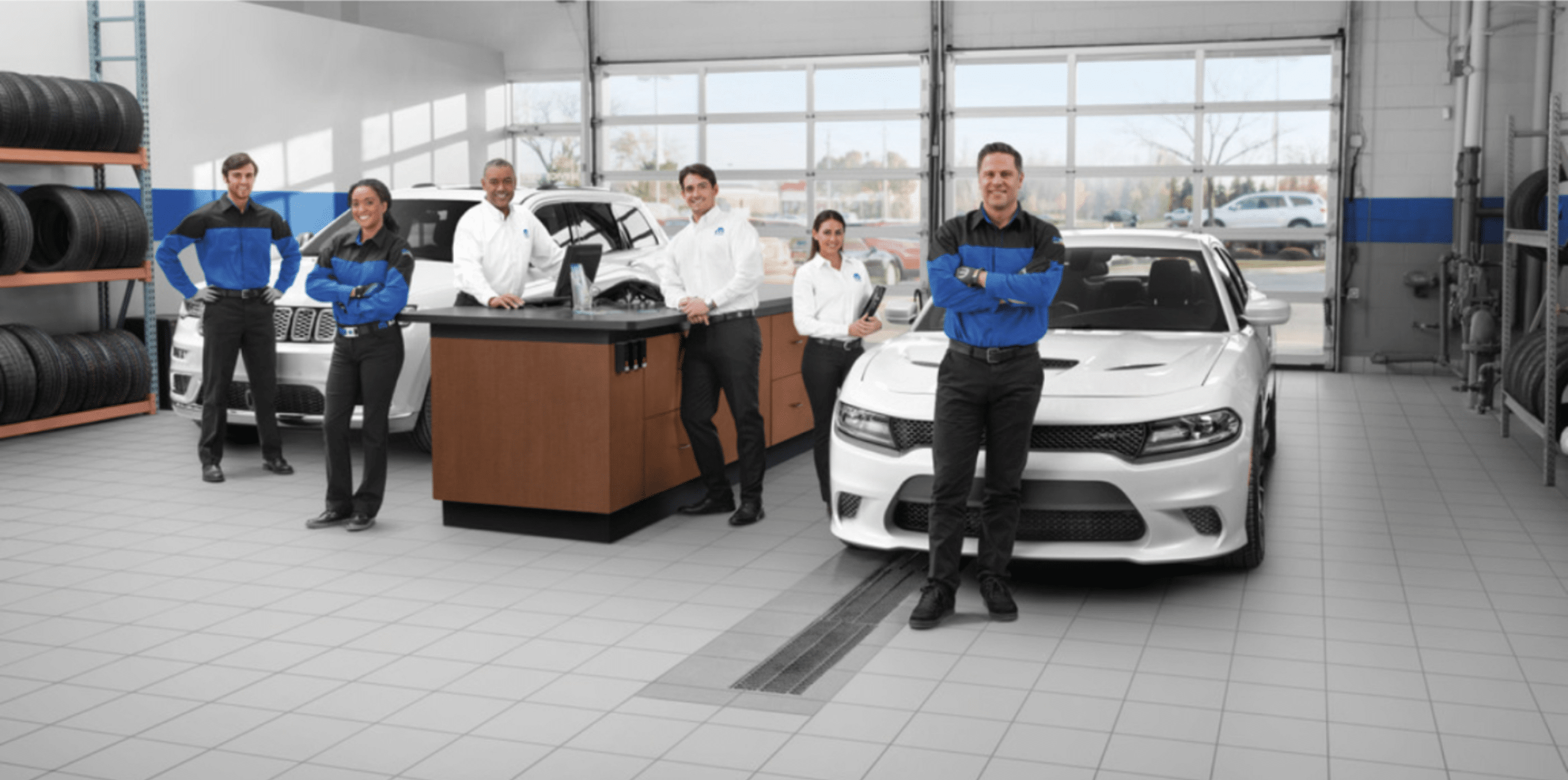 Auto service team in a garage with two cars and tire racks, posing for a group photo.